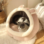 Gato cinza e branco aconchegado em casinha de pelúcia rosa com orelhas de coelho, ideal para descanso e conforto.